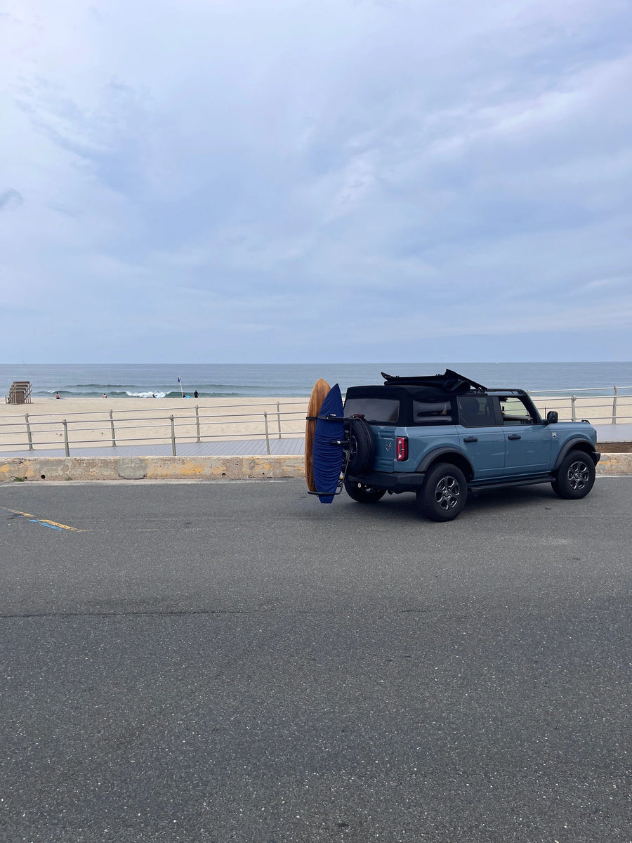 Light blue SUV at beach boardwalk with surfboard